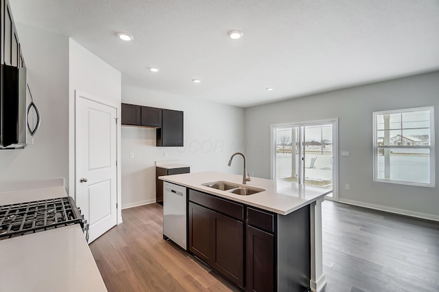 kitchen with stainless steel appliances, a kitchen island with sink, a sink, light wood-type flooring, and light countertops
