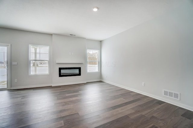 unfurnished living room with baseboards, visible vents, a wealth of natural light, and dark wood finished floors