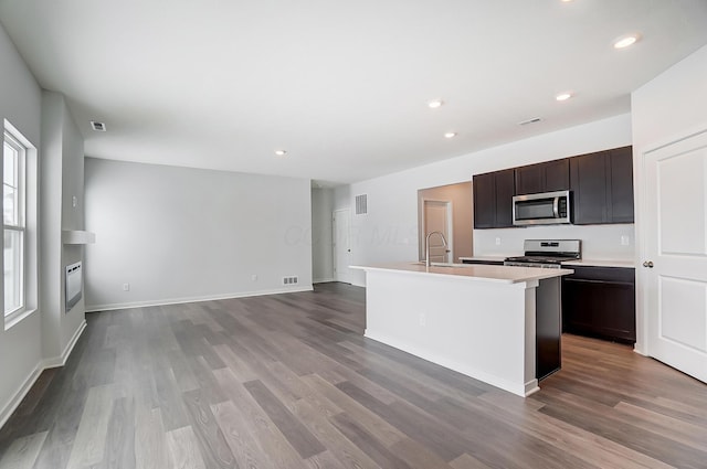 kitchen featuring light countertops, wood finished floors, appliances with stainless steel finishes, and a center island with sink