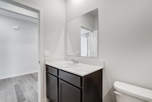 half bath with baseboards, wood finished floors, toilet, and vanity