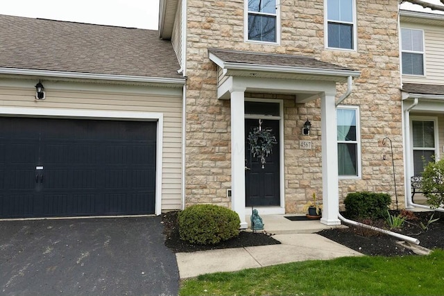 doorway to property featuring aphalt driveway, a shingled roof, an attached garage, and stone siding