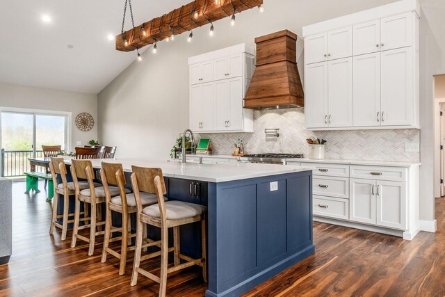kitchen featuring a sink, vaulted ceiling with beams, custom exhaust hood, decorative backsplash, and an island with sink