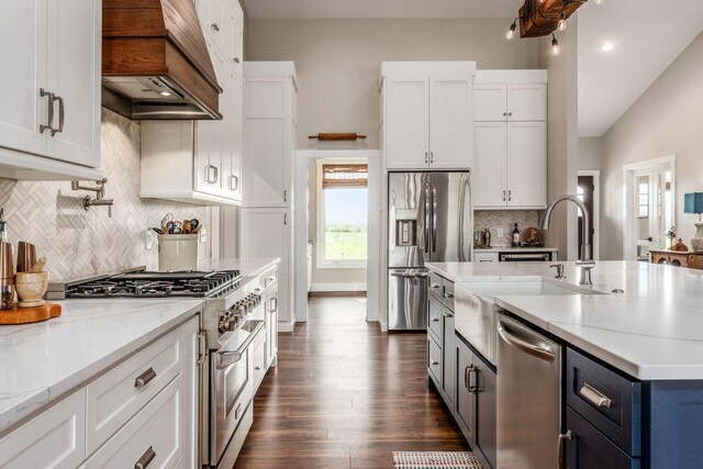 kitchen with tasteful backsplash, light stone counters, white cabinetry, custom range hood, and appliances with stainless steel finishes