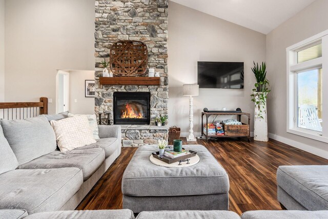 living room with high vaulted ceiling, a stone fireplace, wood finished floors, and baseboards