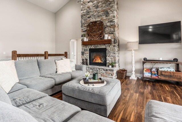 living room featuring baseboards, wood finished floors, high vaulted ceiling, and a stone fireplace