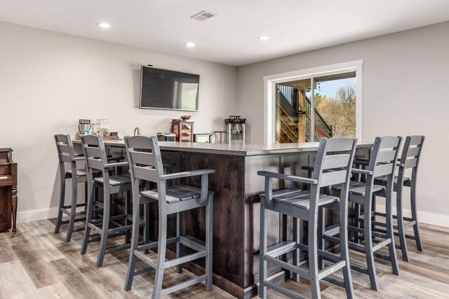 bar with baseboards, a bar, light wood-style floors, and recessed lighting