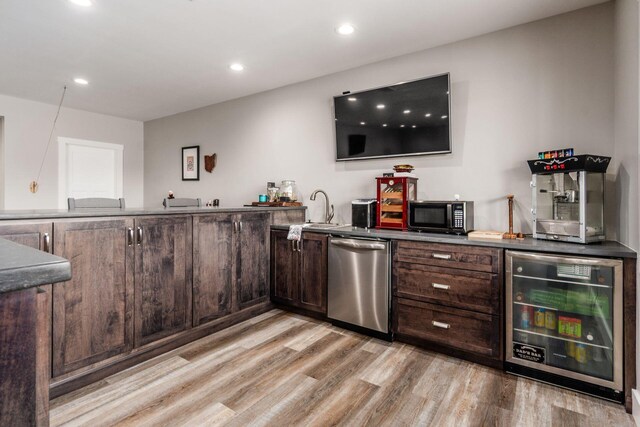 bar featuring a sink, indoor wet bar, light wood-style floors, dishwasher, and beverage cooler