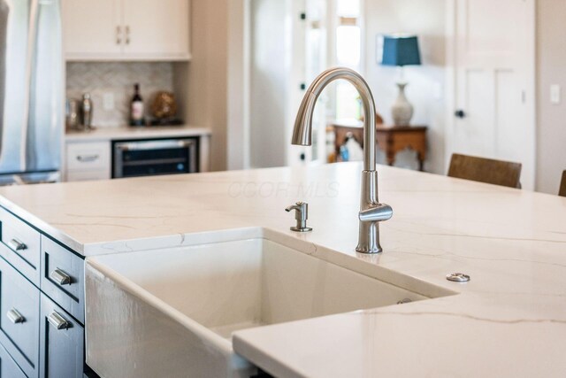 details featuring white cabinetry, beverage cooler, a sink, and light stone countertops