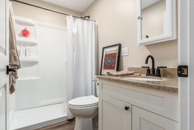 full bath with toilet, wood finished floors, vanity, and a stall shower