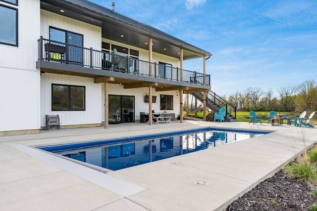 back of house with an outdoor pool, a patio area, stairs, and a balcony