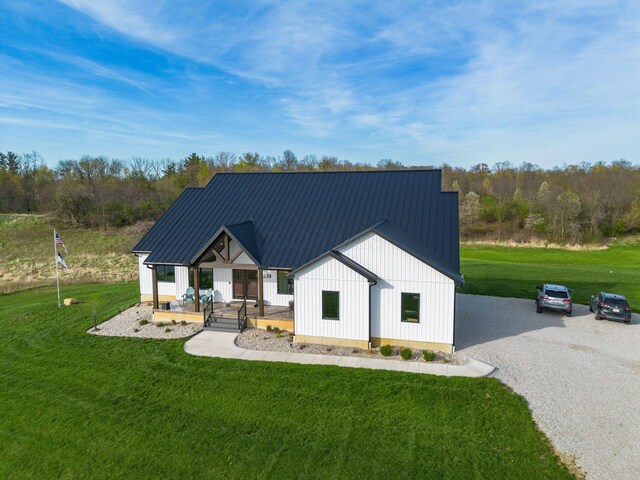 modern inspired farmhouse with board and batten siding, covered porch, metal roof, and a front yard