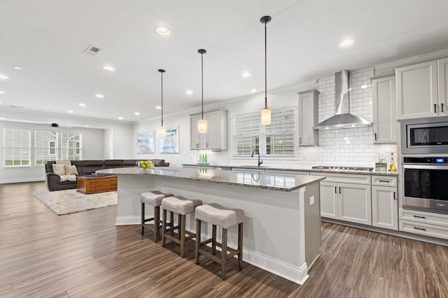 kitchen with a center island, wall chimney exhaust hood, tasteful backsplash, a sink, and stainless steel appliances