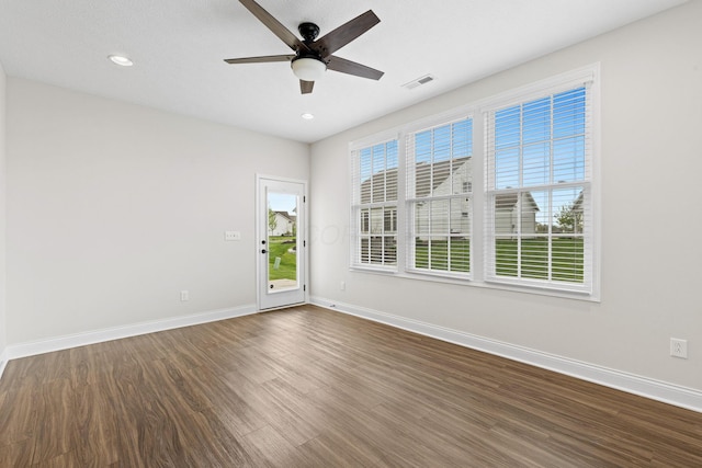 empty room with visible vents, a ceiling fan, baseboards, and dark wood finished floors
