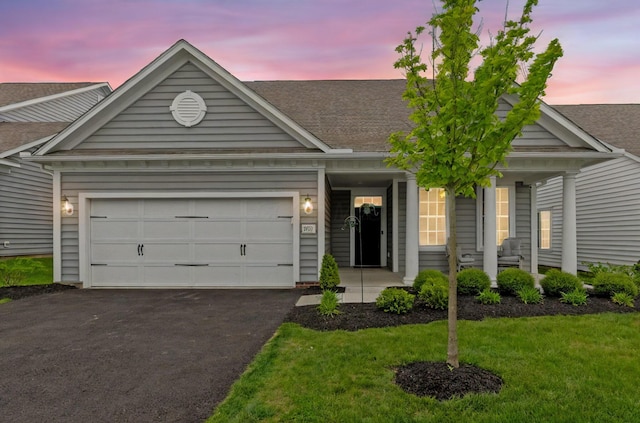 view of front of property with covered porch, aphalt driveway, a yard, an attached garage, and a shingled roof