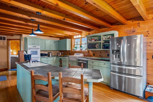 kitchen with green cabinetry, stainless steel appliances, beamed ceiling, and light wood-style floors