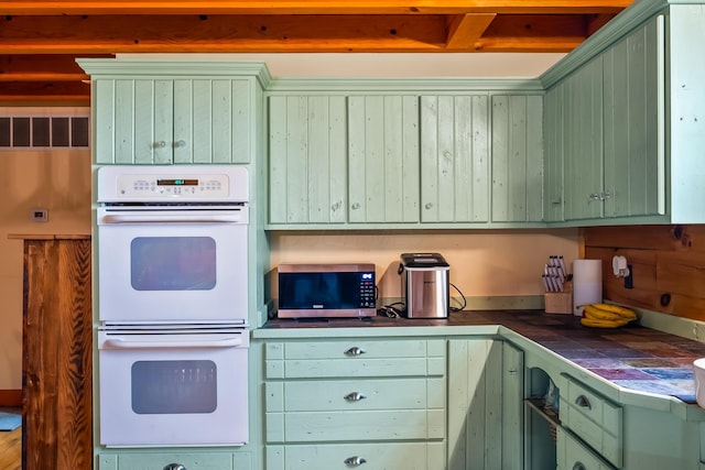 kitchen with double oven, stainless steel microwave, green cabinetry, and tile counters