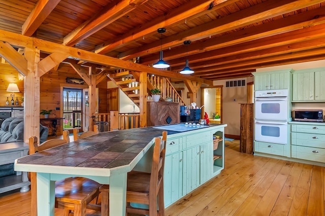 kitchen featuring tile countertops, white double oven, stainless steel microwave, beam ceiling, and visible vents