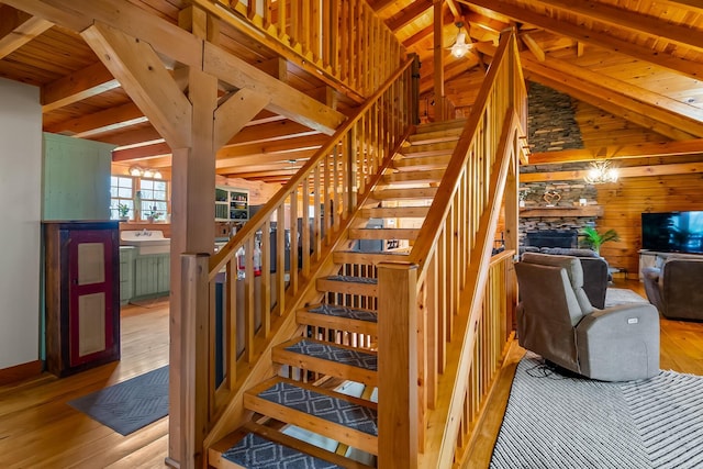 staircase with hardwood / wood-style floors, wooden walls, a stone fireplace, wooden ceiling, and lofted ceiling with beams