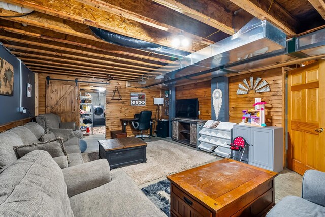 carpeted living area featuring a barn door, wooden walls, and washer and dryer