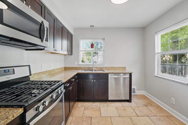 kitchen featuring light stone counters, dark brown cabinetry, stainless steel appliances, and a sink