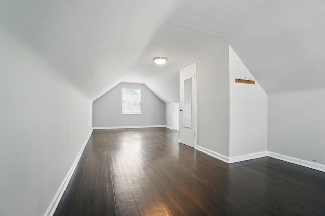 additional living space featuring baseboards, vaulted ceiling, and dark wood-style floors