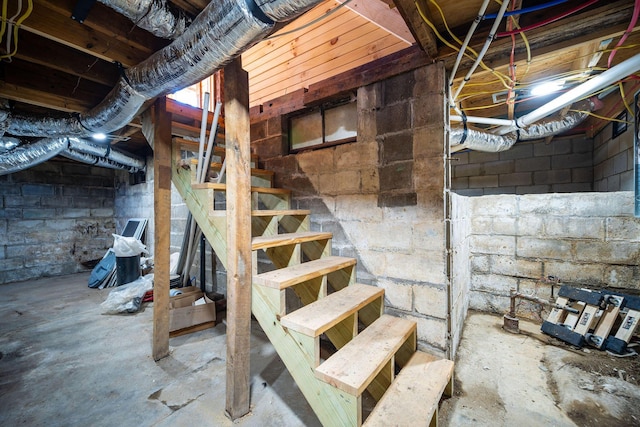 unfinished basement featuring concrete block wall and stairs