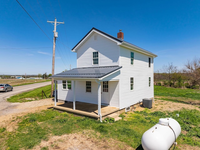 rear view of property featuring a porch, a yard, a chimney, and metal roof