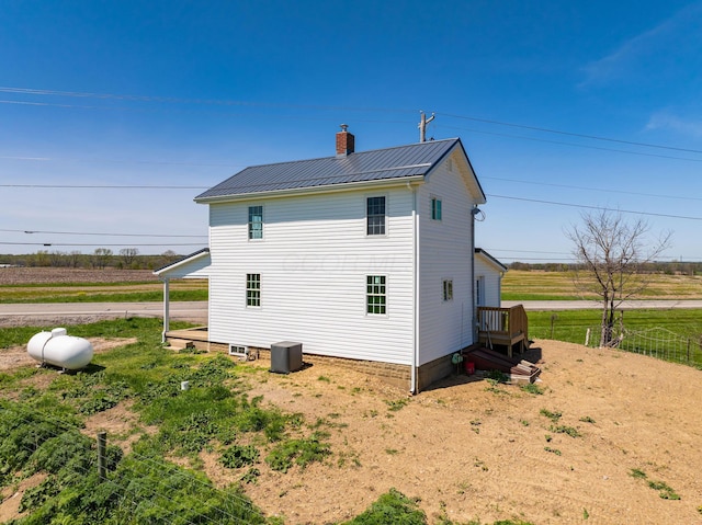 view of property exterior with a chimney, cooling unit, a rural view, a standing seam roof, and metal roof