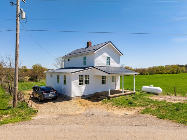view of front of property with a front lawn, covered porch, a chimney, metal roof, and driveway