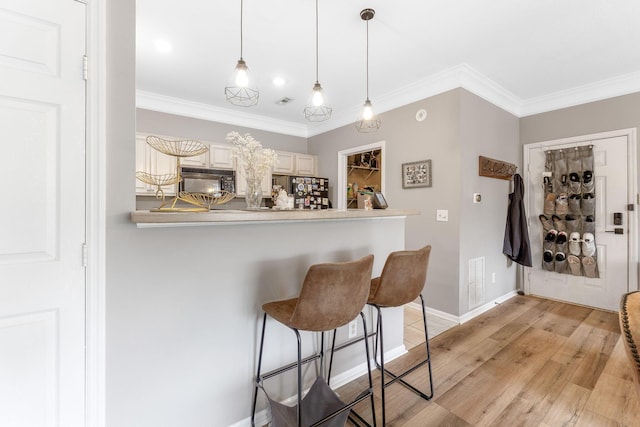 bar with crown molding, hanging light fixtures, black microwave, baseboards, and light wood-type flooring