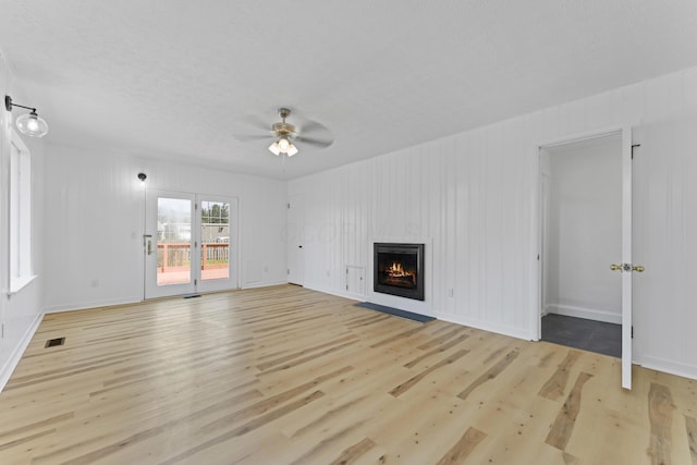 unfurnished living room with light wood finished floors, a warm lit fireplace, visible vents, a ceiling fan, and baseboards