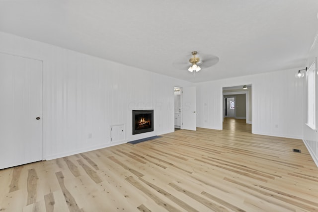 unfurnished living room featuring a ceiling fan, a lit fireplace, visible vents, and light wood-style flooring