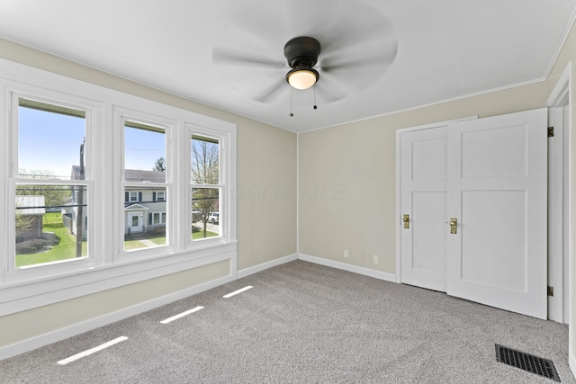 carpeted spare room featuring baseboards, a ceiling fan, and visible vents