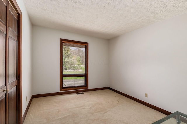 spare room featuring baseboards, visible vents, light carpet, and a textured ceiling