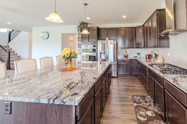 9295 Dewitt Dr, Plain City, OH 43064 - kitchen featuring wall chimney range hood, a large island, appliances with stainless steel finishes, dark brown cabinets, and dark wood-type flooring
