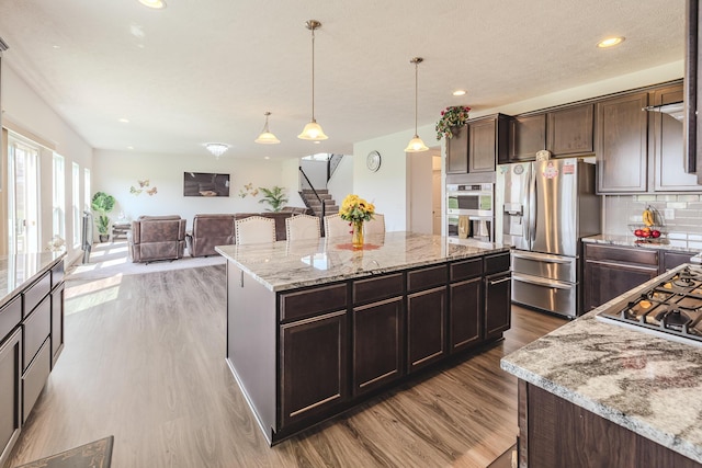 9295 Dewitt Dr, Plain City, OH 43064 - kitchen featuring appliances with stainless steel finishes, light stone countertops, wood finished floors, dark brown cabinets, and open floor plan