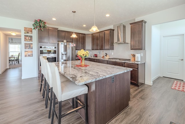 9295 Dewitt Dr, Plain City, OH 43064 - kitchen with a kitchen island, appliances with stainless steel finishes, light wood-type flooring, light stone counters, and wall chimney exhaust hood
