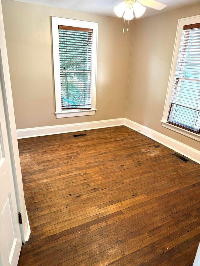 empty room with a healthy amount of sunlight, dark wood-type flooring, and visible vents