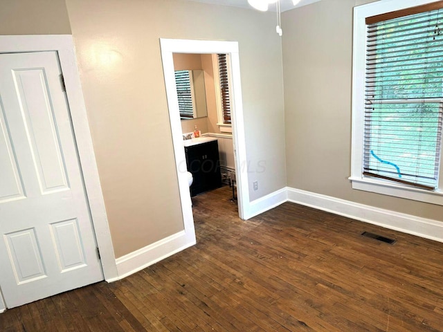 unfurnished bedroom featuring wood-type flooring, visible vents, baseboards, and ensuite bath