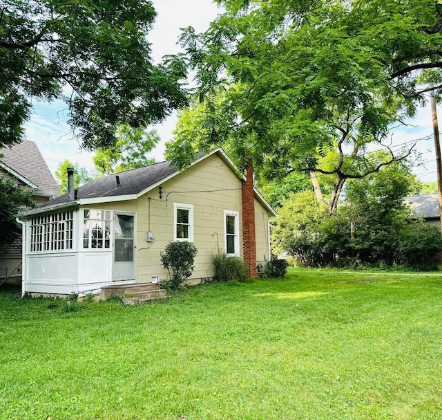 back of house featuring a lawn, a shingled roof, a chimney, and a sunroom