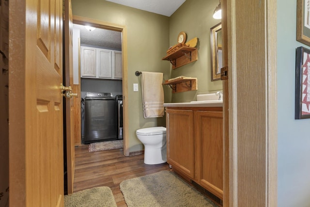 bathroom with independent washer and dryer, toilet, wood finished floors, and vanity