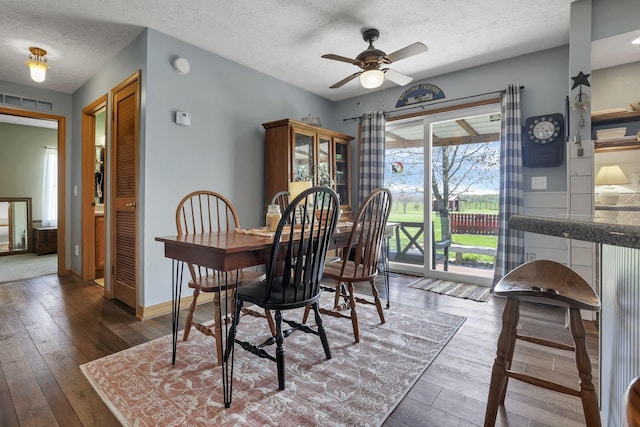 dining area featuring wood-type flooring, a textured ceiling, a ceiling fan, baseboards, and visible vents