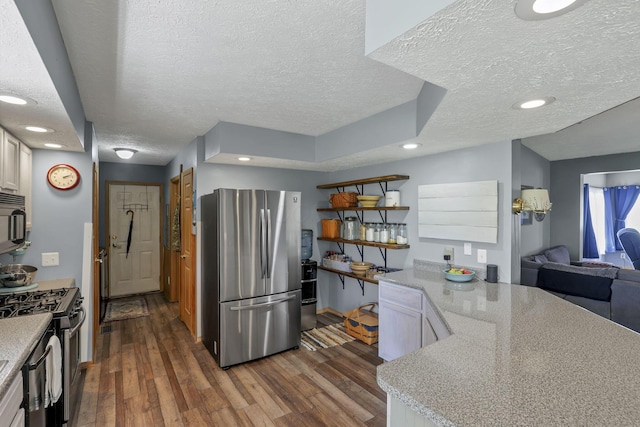 kitchen featuring a peninsula, appliances with stainless steel finishes, dark wood finished floors, and a textured ceiling