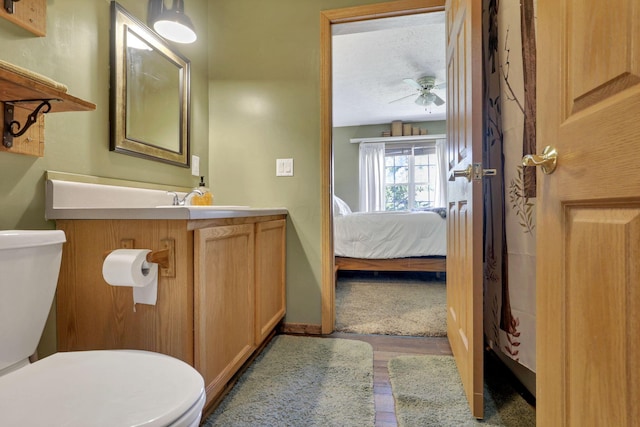 half bath with vanity, wood finished floors, toilet, ceiling fan, and connected bathroom