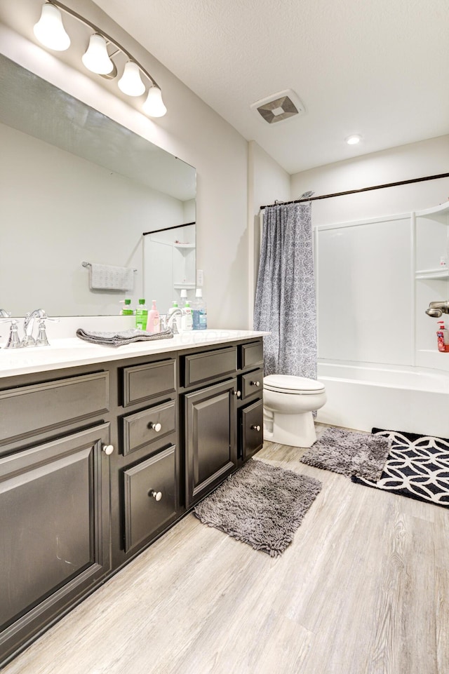bathroom featuring double vanity, toilet, visible vents, shower / bath combo with shower curtain, and wood finished floors