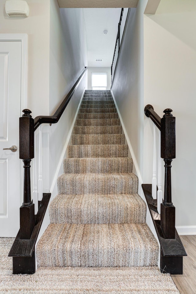 stairway featuring wood finished floors, visible vents, and baseboards