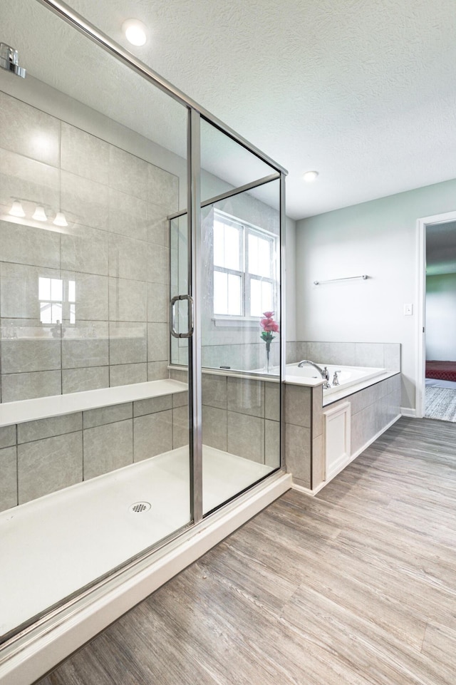 full bathroom featuring a bath, wood finished floors, a textured ceiling, and a stall shower