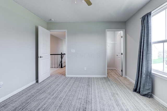 unfurnished bedroom featuring baseboards, a closet, ceiling fan, carpet floors, and a walk in closet