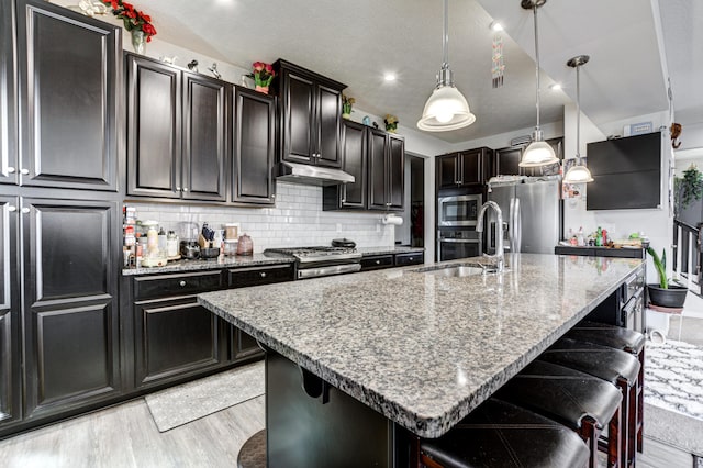 kitchen with light stone countertops, appliances with stainless steel finishes, a breakfast bar area, and a sink
