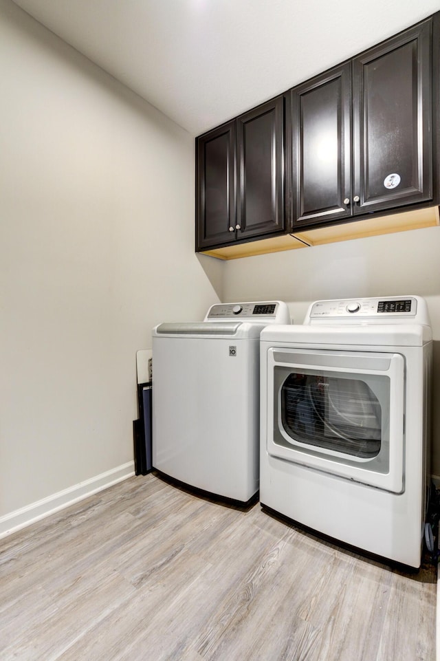 washroom with washing machine and clothes dryer, baseboards, light wood-type flooring, and cabinet space